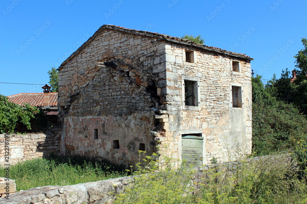 Abandoned stone Mediterranean house surrounded with overgrowth, high uncut grass and stone walls