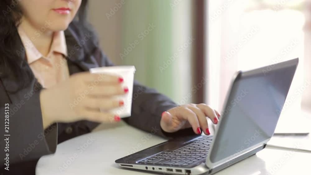 A woman drinks a drink from a disposable cup and works on a laptop. Slow mo. Camera moves A woman drinks a drink from a disposable cup and works on a laptop. Slow mo. Camera moves