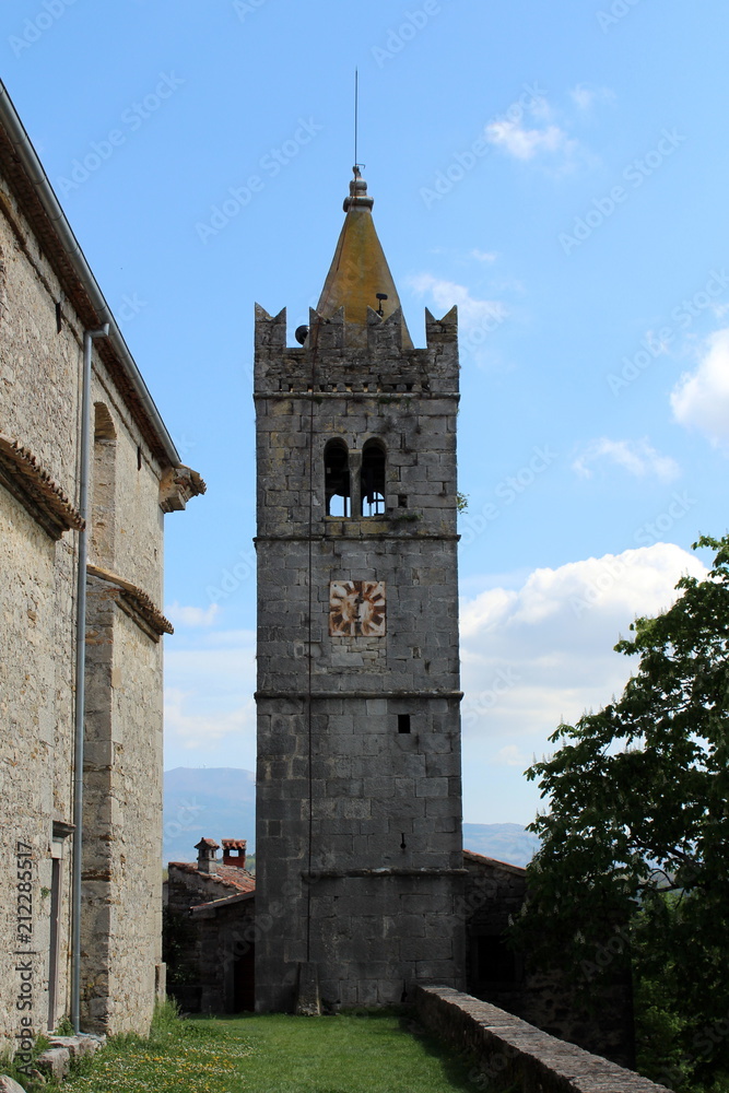 Large stone bell tower with yellow top and rusted old metal clock in the middle