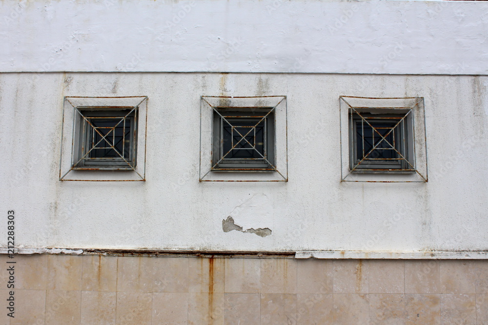 Three wooden frame rectangle glass windows with partially rusted metal bars mounted on dilapidated wall outside Three wooden frame rectangle glass windows with partially rusted metal bars mounted on dilapidated wall outside