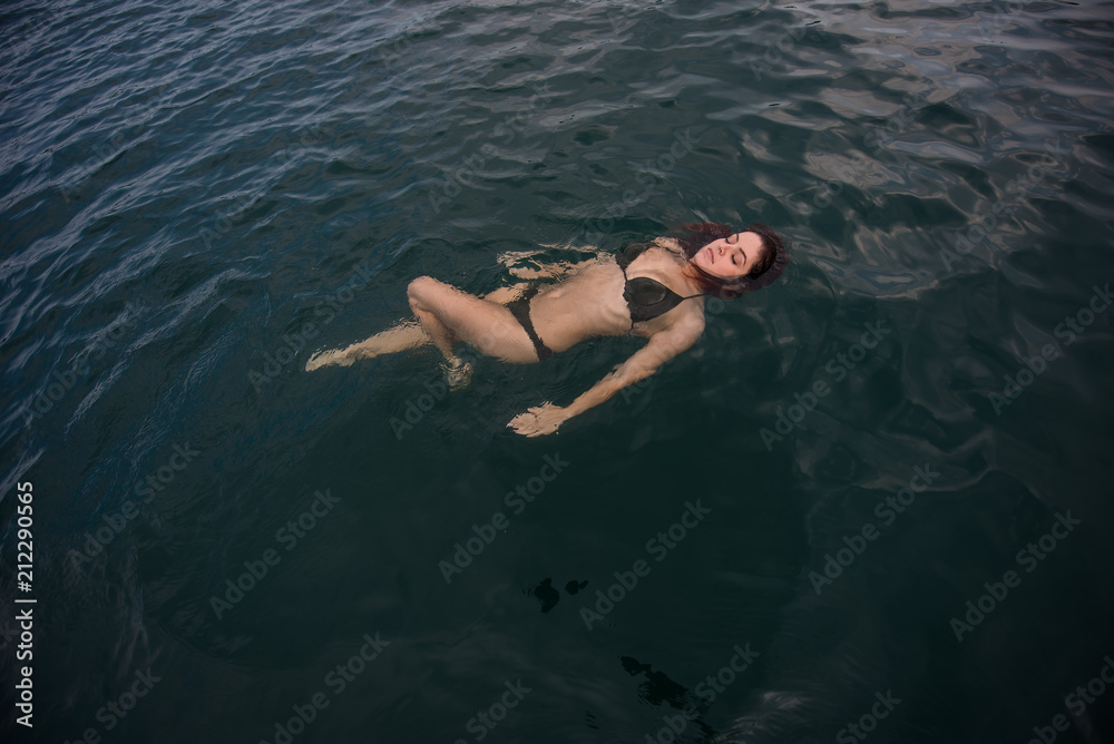 Young woman lies in the water on her back. Beautiful woman in a green bikini is lying on her back in the water.
