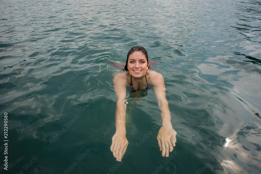 Young woman lies in the water on her back. Beautiful woman in a green bikini swimming in the lake