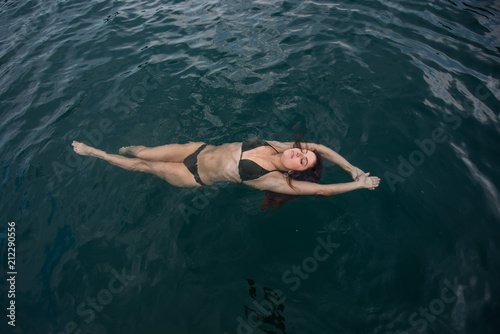 Young woman lies in the water on her back. Beautiful woman in a green bikini is lying on her back in the water.