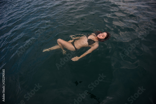 Young woman lies in the water on her back. Beautiful woman in a green bikini is lying on her back in the water. © Михаил Решетников