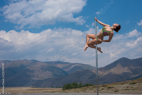 woman dancing on a pole among the mountains. young girl pole dancing out of doors