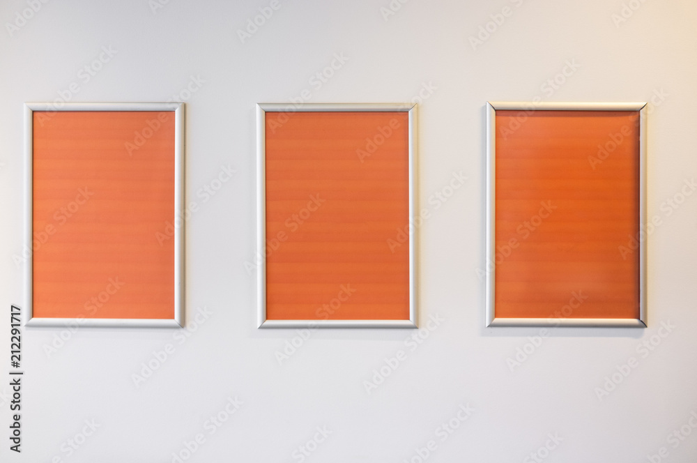 Three picture frames with orange copy space hanging on white wall