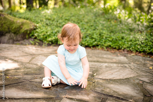 Sweet little girl playing with water puddle on stone path at the park