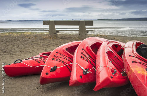 Empty red plastic recreational kayaks for rent or hire, stored on sandy beach after hours on a rainy day. Crescent Beach, Surrey, British Columbia, Canada. © illuminaphotographic