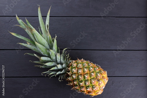 Pineapple on wooden boards, pineapple with leaves on black background, tropical fruit with copy space, blank for designer, vegetarian food, fruit for salad preparation, art