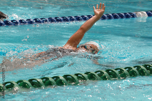 Asian girl with white cap swims backstroke or back crawl in a swimming pool for competition or race