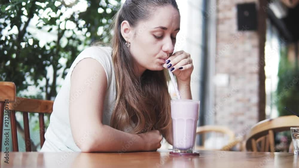Young beautiful european girl drinks cold milk cocktail with blueberry in a cafe in hot summer day. Women drinking smoothies throught the straw. Young beautiful european girl drinks cold milk cocktail with blueberry in a cafe in hot summer day. Women drinking smoothies throught the straw.