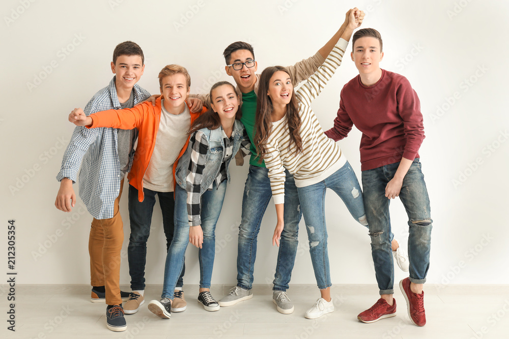 Group of cute teenagers standing near white wall