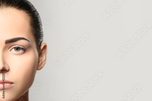 Young woman with permanent eyebrows makeup on grey background