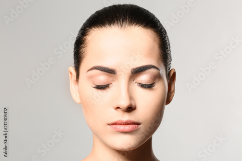 Young woman with permanent eyebrows makeup on grey background