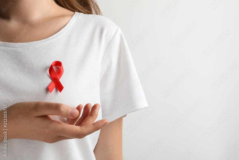 Woman with red ribbon on t-shirt against light background. Cancer awareness Woman with red ribbon on t-shirt against light background. Cancer awareness