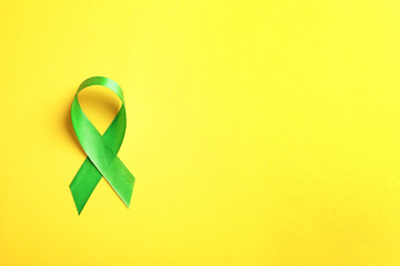 Green ribbon on color background, top view. Cancer awareness