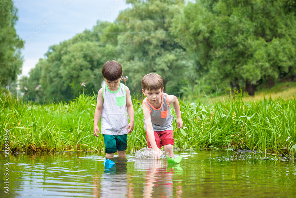 Two little brothers playing with paper boats by a river on warm and sunny summer day. Two little brothers playing with paper boats by a river on warm and sunny summer day.