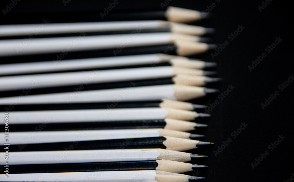 The row of graphite sharpened black and white pencils close up on black background. The row of graphite sharpened black and white pencils close up on black background.