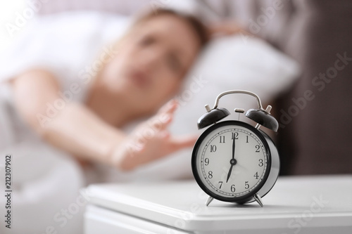 Alarm clock on table and woman in bedroom. Sleeping time