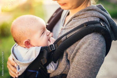 Little baby girl and her mother walking outside during sunset. Mother is holding and tickling her baby, babywearing in the carrier photo