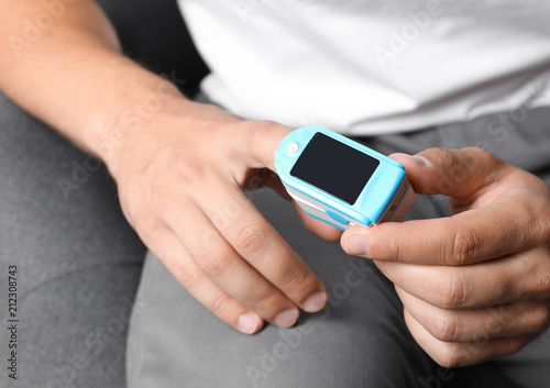 Young man checking pulse with blood pressure monitor on finger, closeup