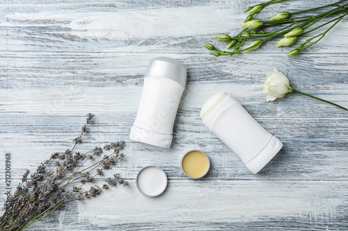 Flat lay composition with different deodorants and flowers on wooden background photo