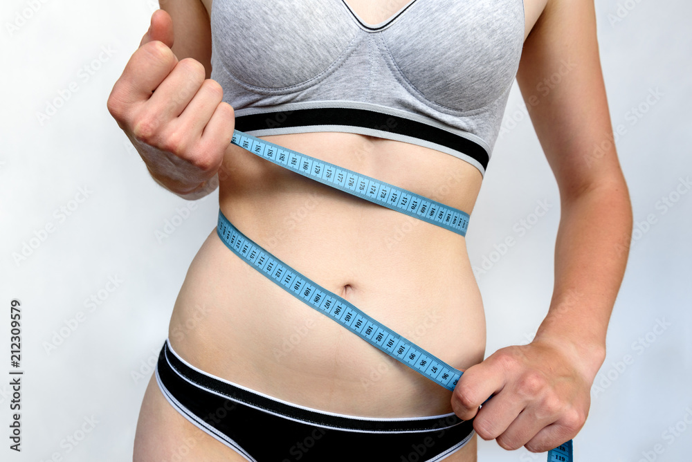 Photo of Young slim woman measuring her waist with a tape