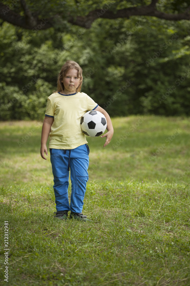 Little child soccer player. Boy with ball on green grass