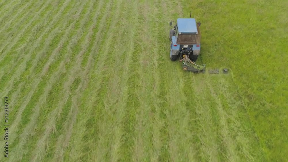 Tractor mowing grass with a disc mower for animal feed. Aerial view Preparation feed silage with mower mounted on tractor. Tractor mowing grass with a disc mower for animal feed. Aerial view Preparation feed silage with mower mounted on tractor.