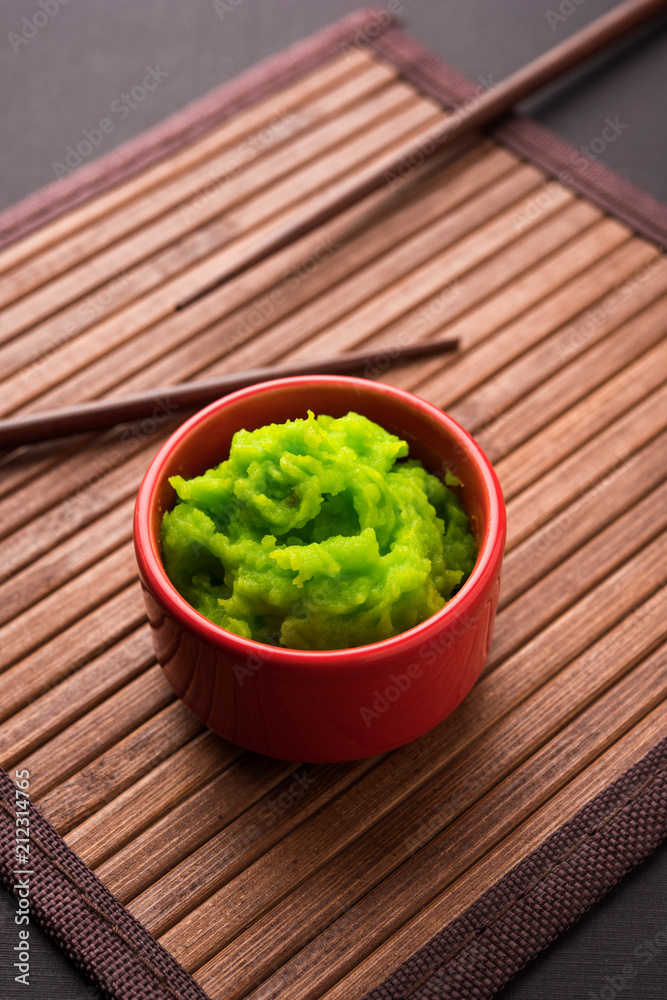 Green wasabi sauce or paste in bowl, with chopsticks or spoon over plain colourful background. selective focus Green wasabi sauce or paste in bowl, with chopsticks or spoon over plain colourful background. selective focus