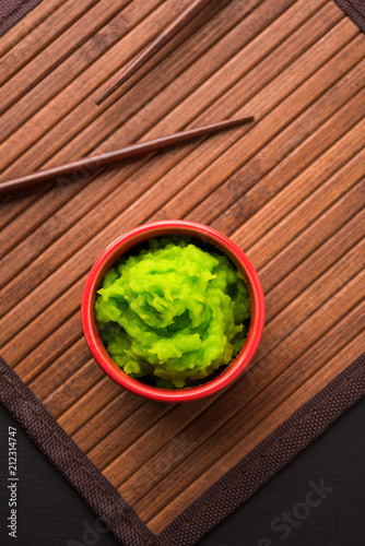 Green wasabi sauce or paste in bowl, with chopsticks or spoon over plain colourful background. selective focus