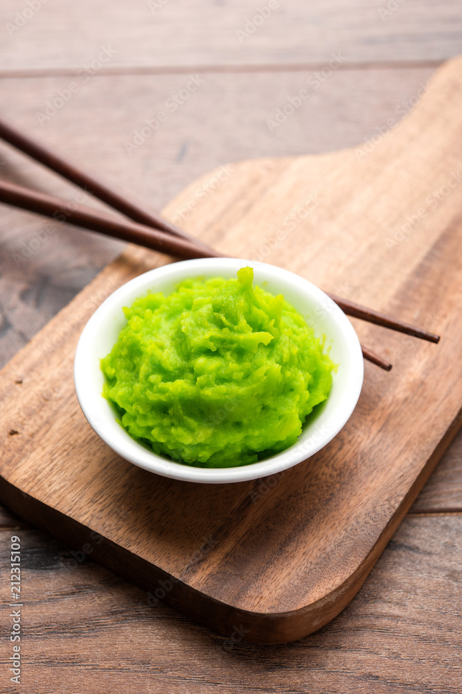 Green wasabi sauce or paste in bowl, with chopsticks or spoon over plain colourful background. selective focus Green wasabi sauce or paste in bowl, with chopsticks or spoon over plain colourful background. selective focus