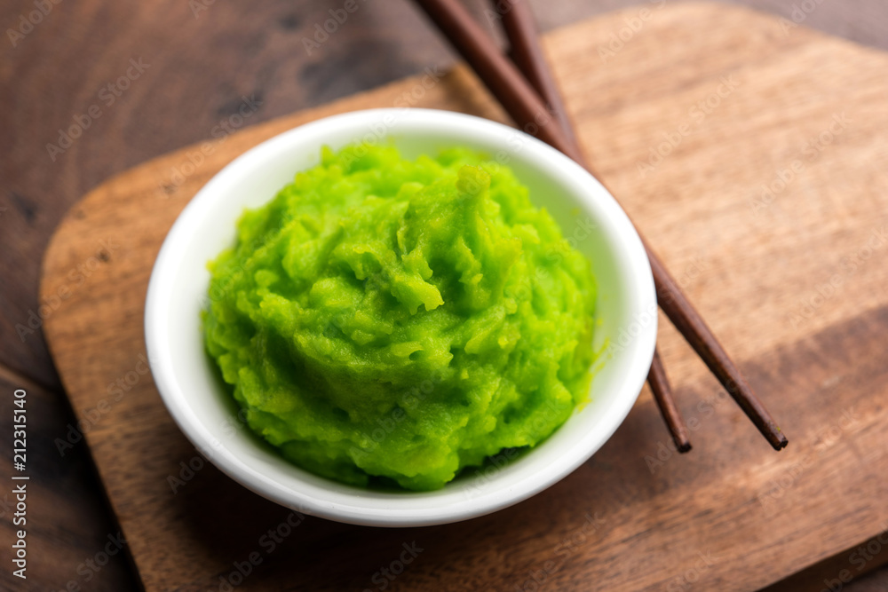 Green wasabi sauce or paste in bowl, with chopsticks or spoon over plain colourful background. selective focus Green wasabi sauce or paste in bowl, with chopsticks or spoon over plain colourful background. selective focus