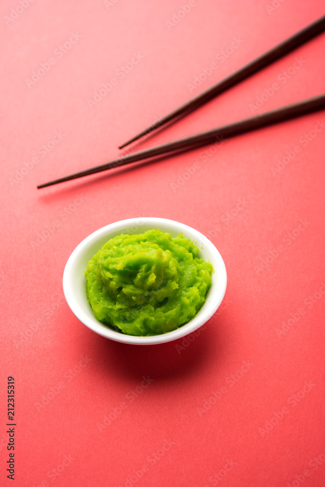 Green wasabi sauce or paste in bowl, with chopsticks or spoon over plain colourful background. selective focus Green wasabi sauce or paste in bowl, with chopsticks or spoon over plain colourful background. selective focus