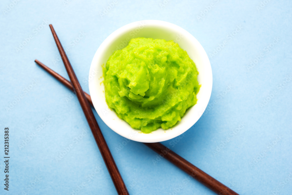 Green wasabi sauce or paste in bowl, with chopsticks or spoon over plain colourful background. selective focus Green wasabi sauce or paste in bowl, with chopsticks or spoon over plain colourful background. selective focus