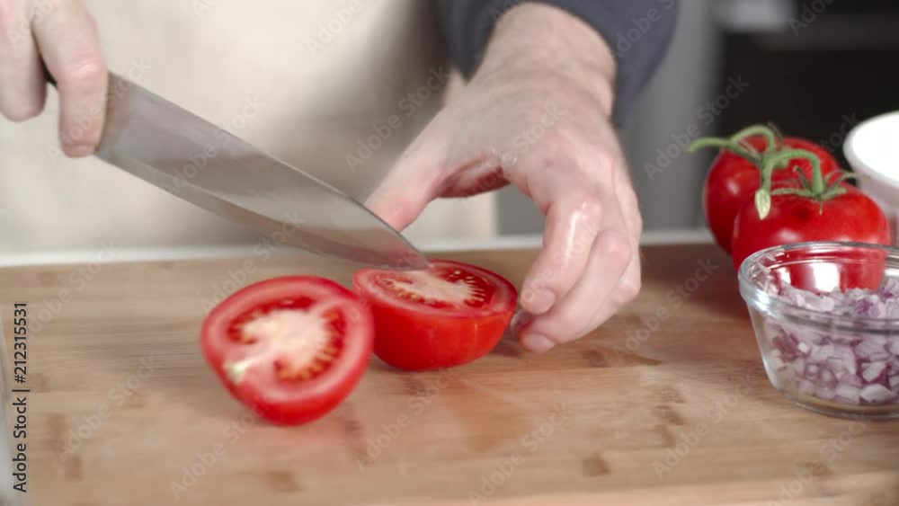 Slow-mo dolly shot of chef slicing ripe tomato with large kitchen knife Slow-mo dolly shot of chef slicing ripe tomato with large kitchen knife