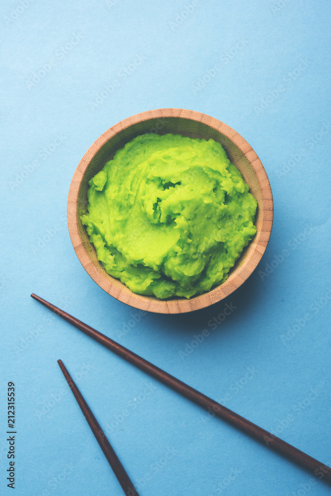 Green wasabi sauce or paste in bowl, with chopsticks or spoon over plain colourful background. selective focus