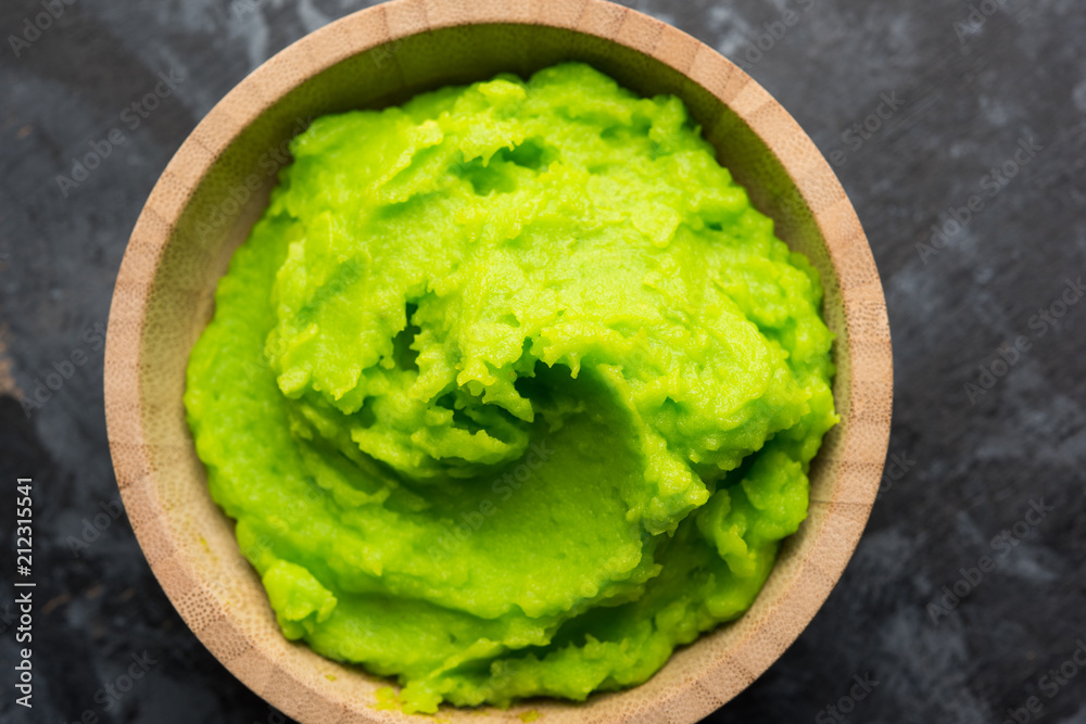 Green wasabi sauce or paste in bowl, with chopsticks or spoon over plain colourful background. selective focus Green wasabi sauce or paste in bowl, with chopsticks or spoon over plain colourful background. selective focus