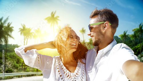 Two young lovers on summer trip and background with palms and sun light.  © magdal3na