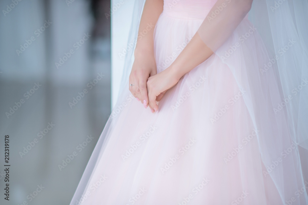 Bride holds her hands crossed down on the pink scirt Bride holds her hands crossed down on the pink scirt