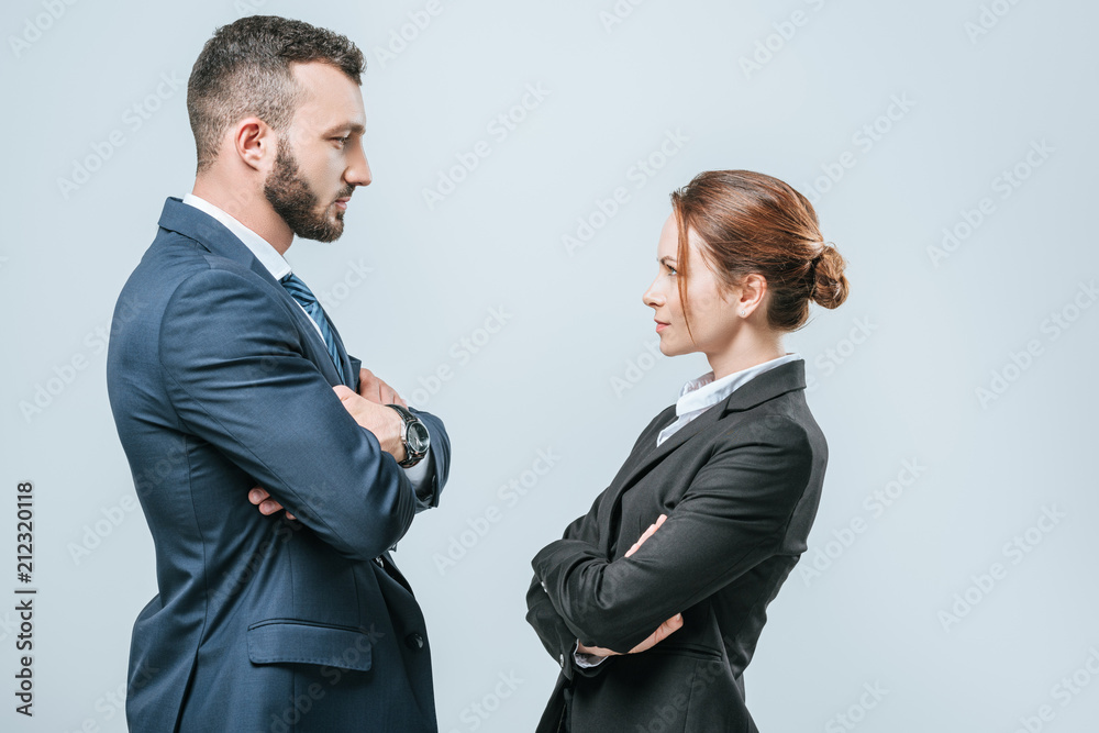 businesswoman and businessman standing with crossed arms and looking at each other isolated on grey