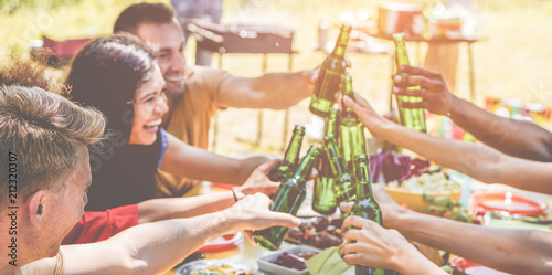 Happy millennial friends cheering with beers at barbecue party in nature
