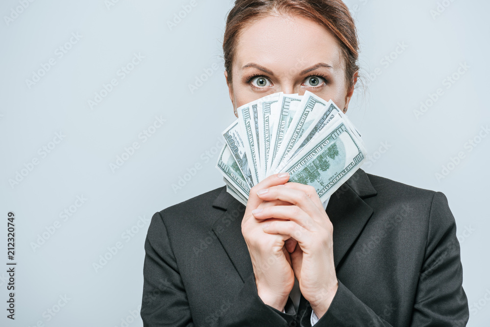 attractive financier looking out from pack of dollar banknotes isolated on grey attractive financier looking out from pack of dollar banknotes isolated on grey