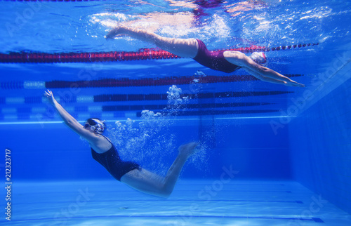 Two young girls swim underwater in the pool