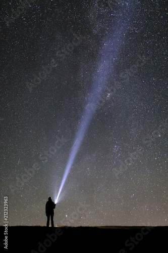 Silhouette of a tourist with a flashlight, observing beautiful, wide blue night sky with stars and galaxies