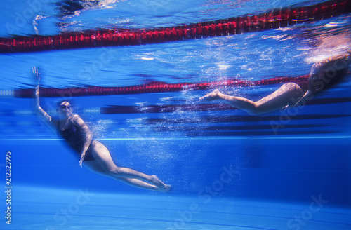 Two young girls swim underwater in the pool