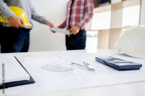 Engineers discuss a blueprint while checking information on a tablet computer in a office.