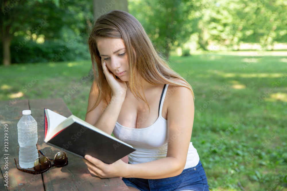 Obraz premium Teenage girl reading a book sitting in the park