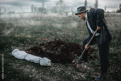 Killer is digging a grave for the victim in forest photo