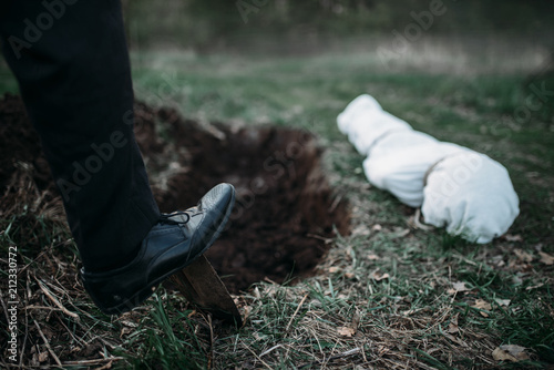 Male murderer with a shovel  is digging a grave photo